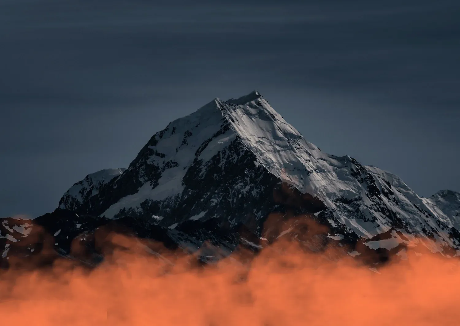 a large rocky mountain with snow on it. gray-blue nightime sky in the background, foggy, starless. a giant scarlet cloud, perhaps wildfire smoke, sits at the bottom of the mountain in stark contrast to the cool undertones of the rest of the picture. it's as if the mountain is sitting on top of the cloud